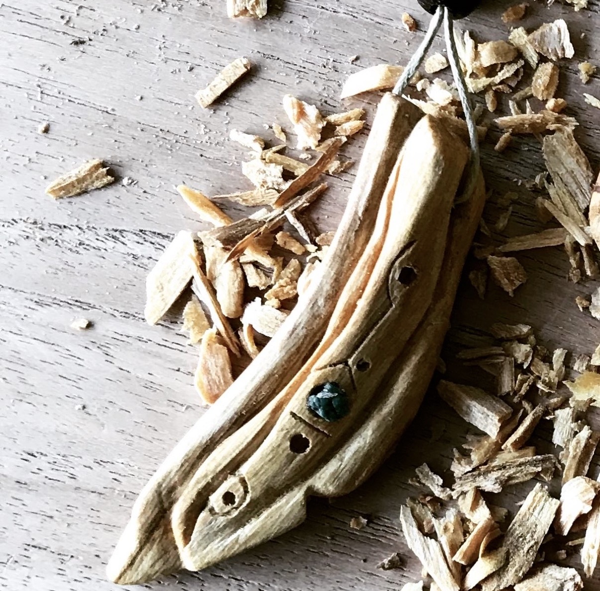 Handgesneden amulet van Palo Santo met een ruwe edelsteen, tussen de houtkrullen