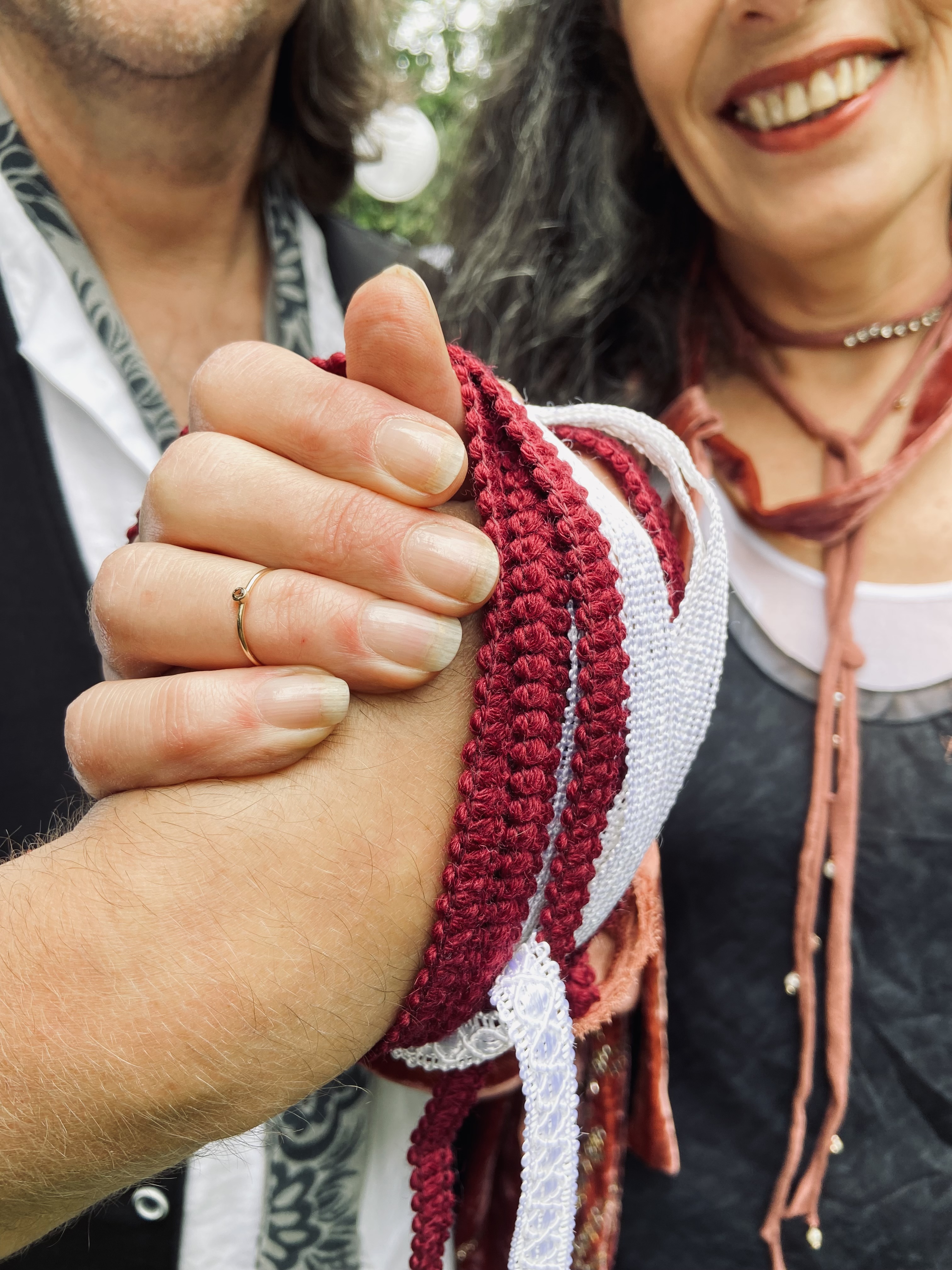 Twee handen verbonden met rode en witte koorden tijdens een handfasting